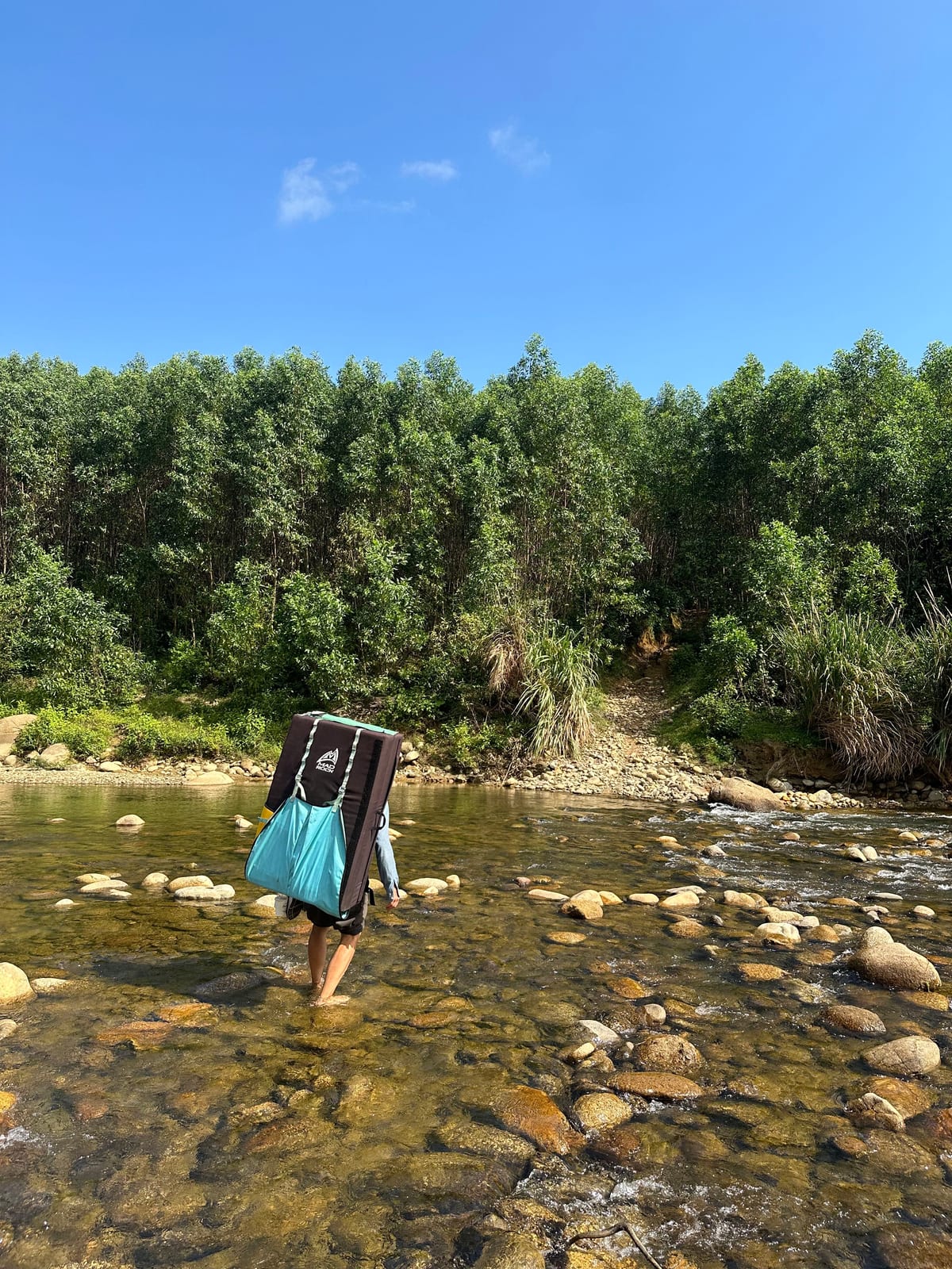 Climber carrying a crash pad across the river on the approach to the Ba Na Hills boulders