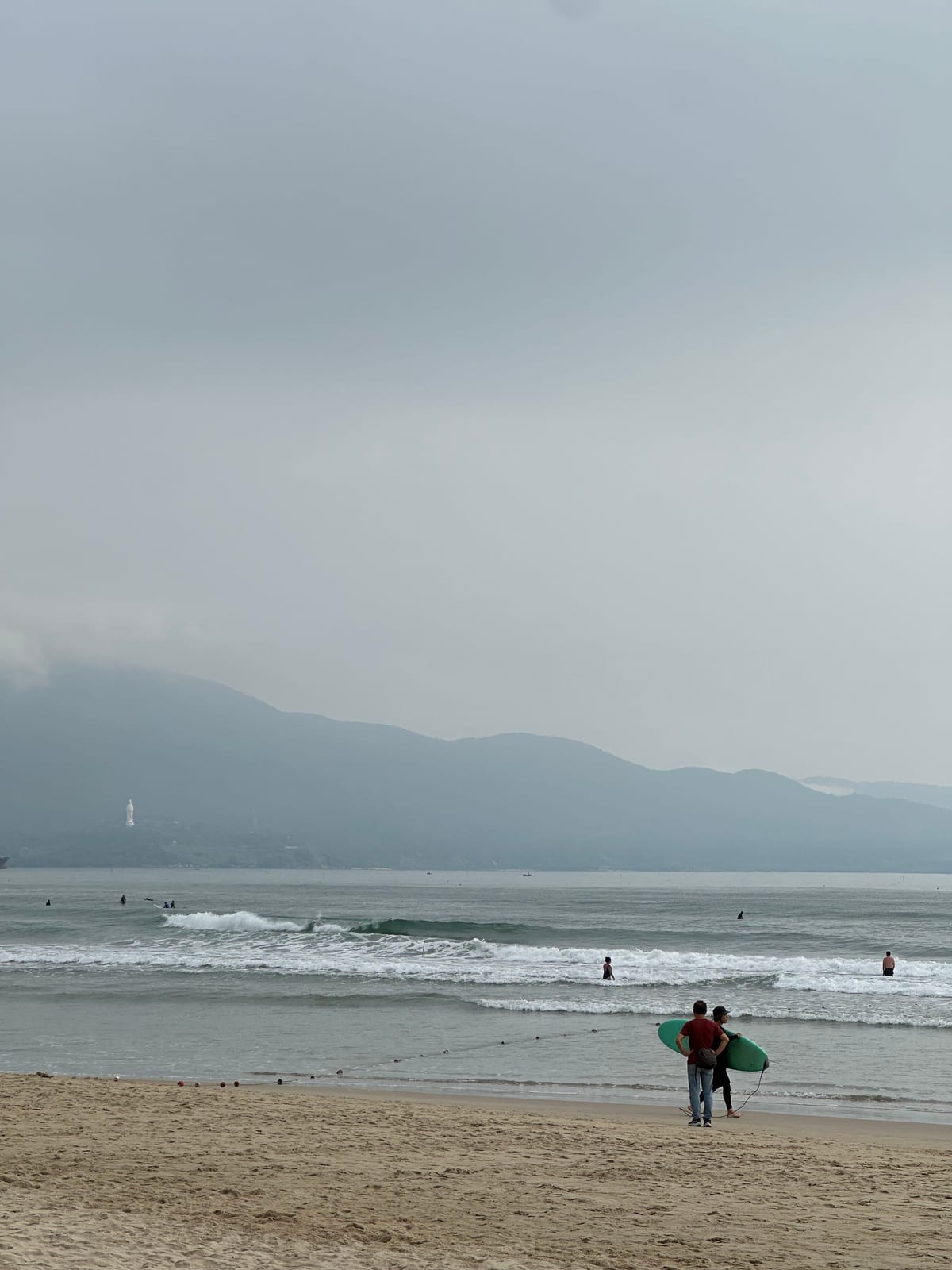 Surfers walking out at My Khe beach with the Son Tra peninsula behind, Da Nang