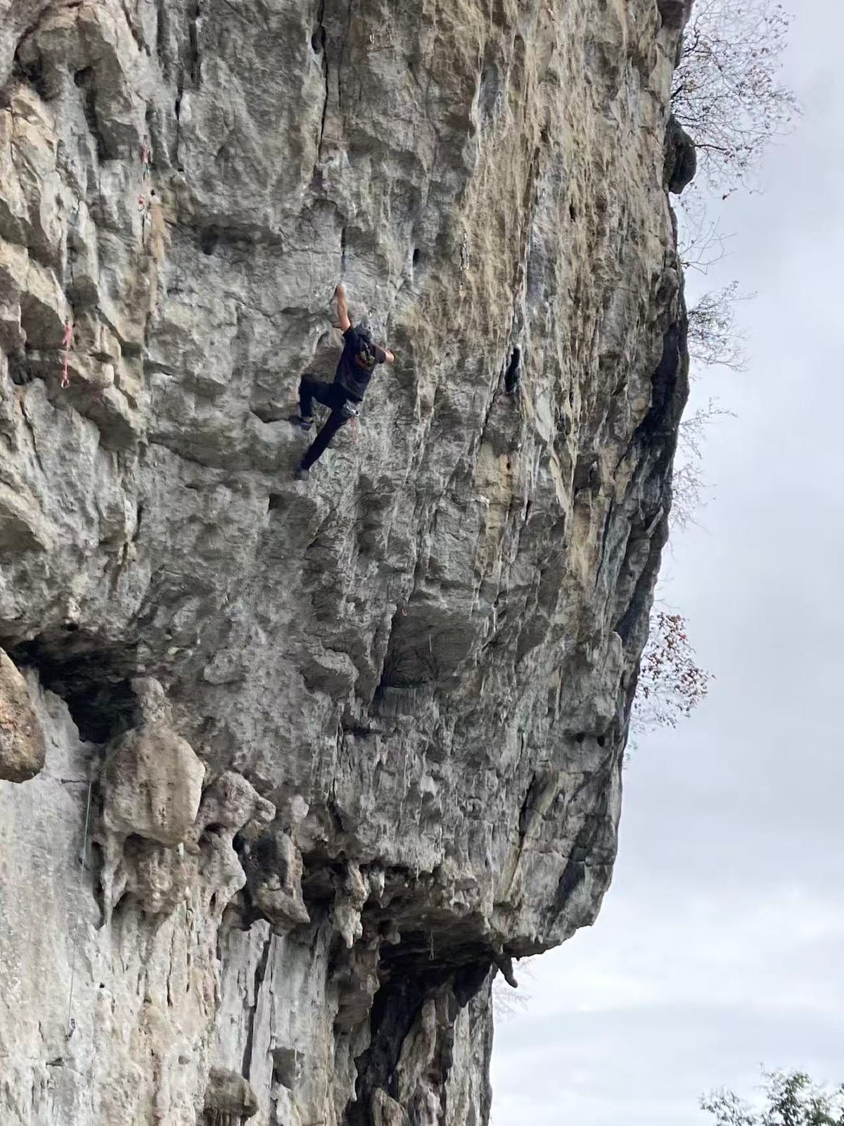 Climber at the upper crux of Dragonfly 7a+ on the steep wall at Riverside, Yangshuo