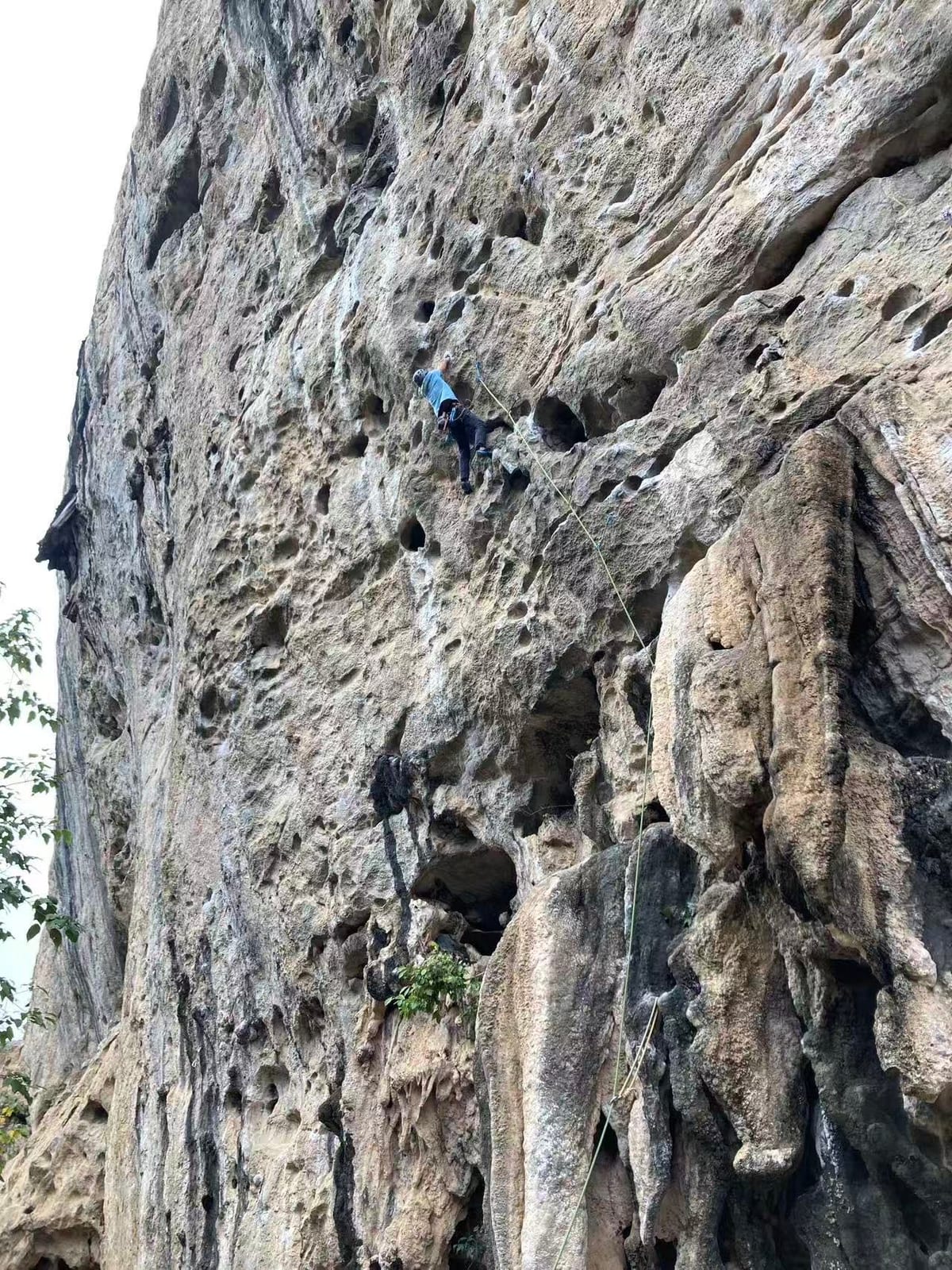 Climber high on the upper wall of a 7a route at White Mountain, Yangshuo