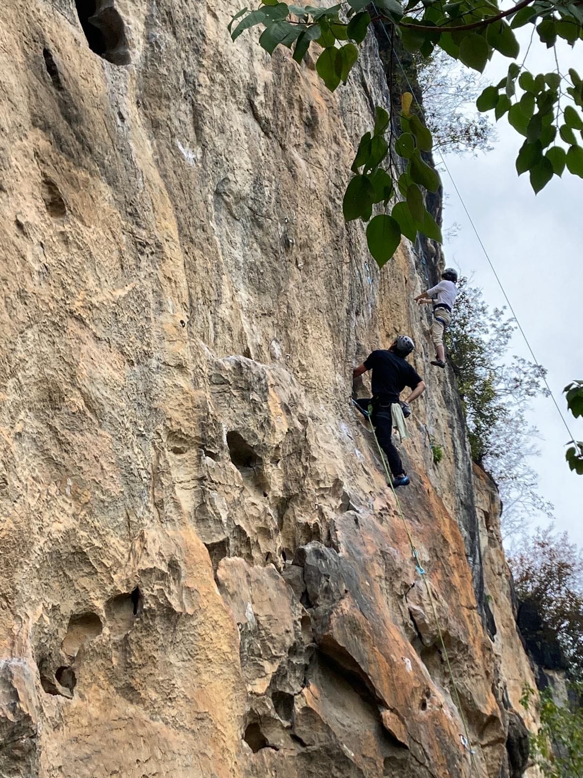 Climber pulling on pockets in orange limestone at White Mountain crag, Yangshuo