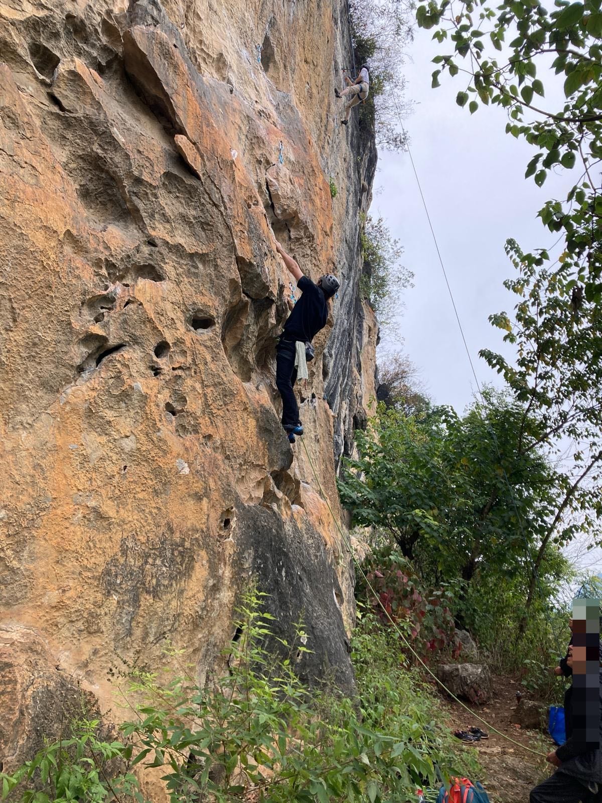 Climber on a steep orange limestone sport route at White Mountain, Yangshuo